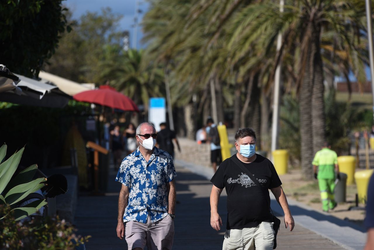 Tourists wearing face masks as a preventive measure walk along Somorrostro beach during the coronavirus crisis.
