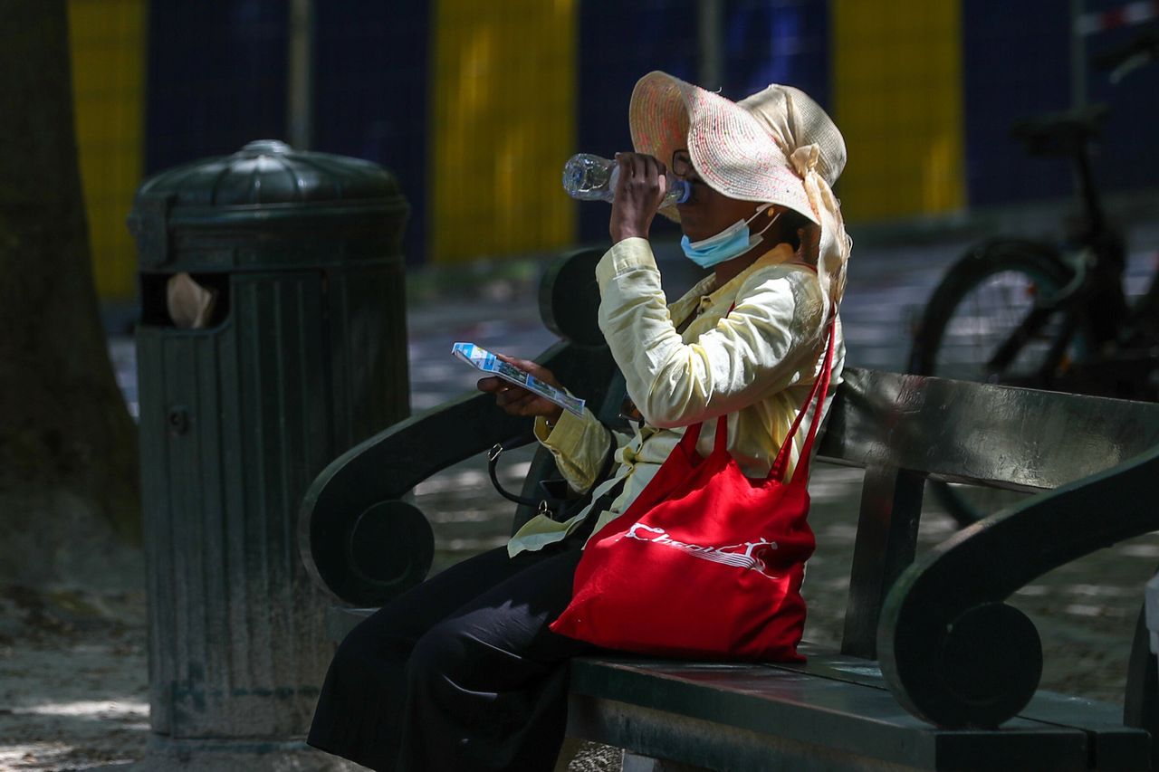 A woman drinks water as she sits on a bench during a heatwave, in Brussels, Belgium.