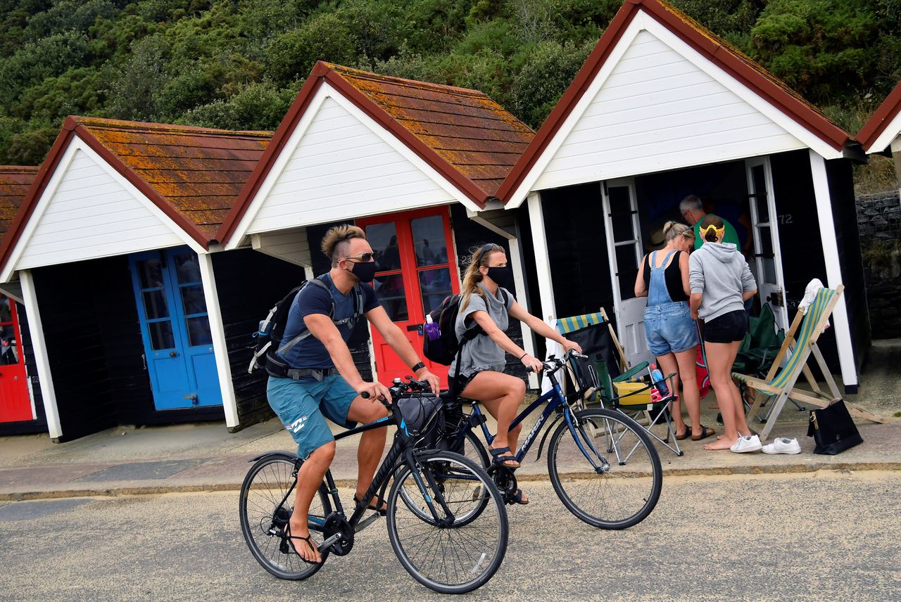 People wear protective face masks as they cycle along the seafront past the beach huts in Bournemouth.
