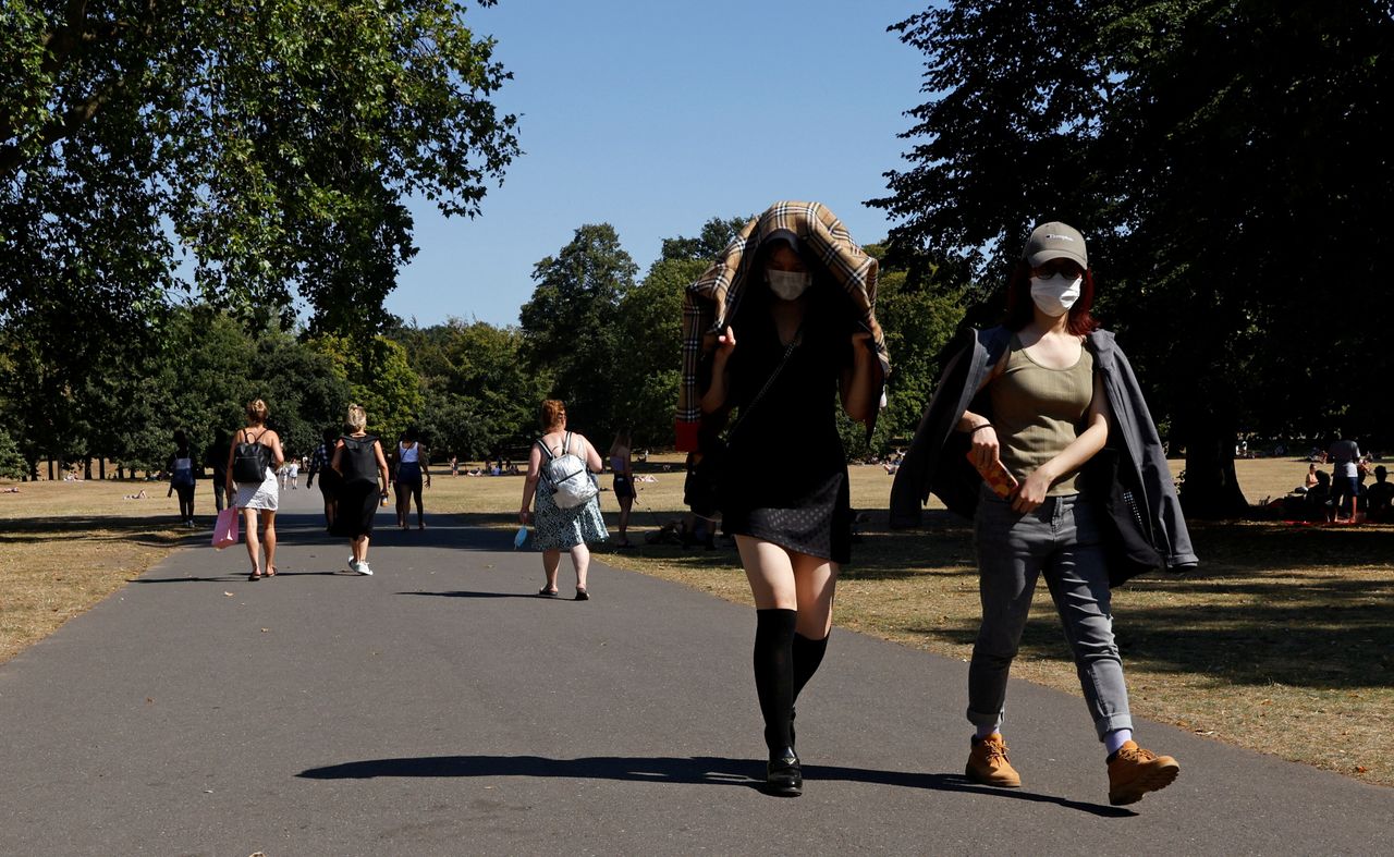 People shield themselves from the sun as they walk through Greenwich Park.