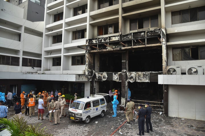 Rescuers and others stand outside Hotel Swarna Palace where a fire broke out early morning in Vijayawada, Andhra Pradesh stat