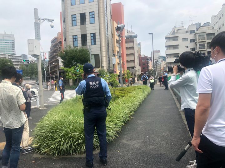 カルガモの親子を見守る警察官やメディア。カルガモの一行は、中央の茂みで一休み＝東京都港区、2020年7月25日