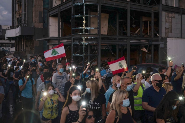 Demonstrators march past a damaged building holding candles and flashlights honoring the victims of the deadly explosion at Beirut port which devastated large parts of the capital, in Beirut, Lebanon, Sunday, Aug. 9, 2020. (AP Photo/Felipe Dana)