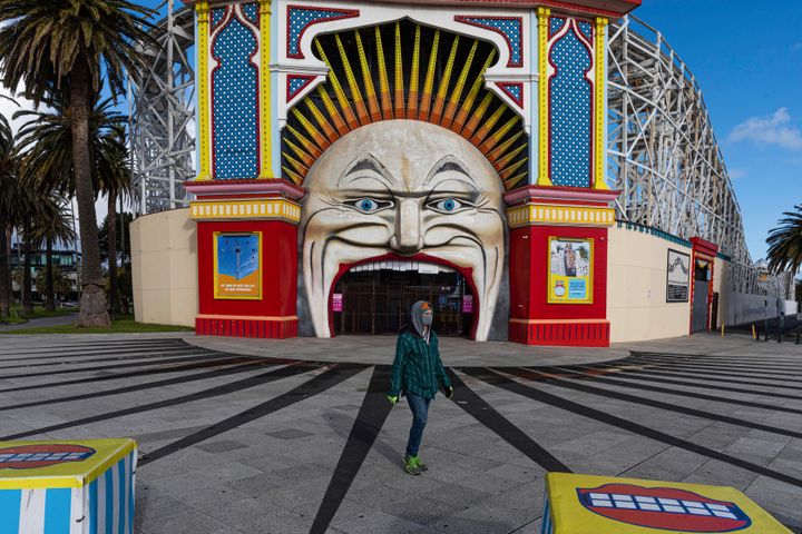 A man wearing a mask walks past Luna Park in the suburb of St Kilda during lockdown in Melbourne, Australia, Wednesday, Aug. 5, 2020. (AP Photo/Asanka Brendon Ratnayake)