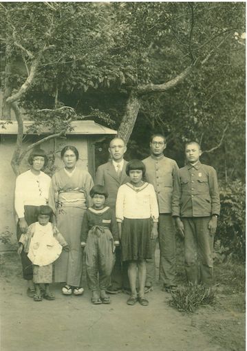 萬井家の家族写真。真ん中の白いセーラー服を着ているのが頌子さん。 とみさん（左上2番目）、美夫さん（右上2番目）、珍男さん（右端）