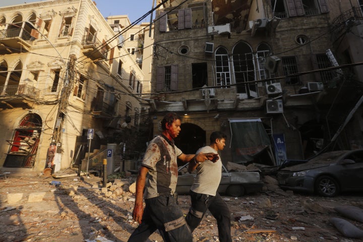 A wounded man is helped as he walks through debris.