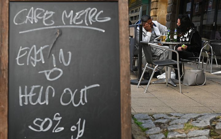 Diners sit at table near a sign promoting the British Government's "Eat out to Help out" COVID-19 scheme to get consumers spending again, outside a restaurant in Manchester, northwest England on August 3, 2020, - Britain's "Eat out to Help out" scheme began Monday, introduced last month by Chancellor Rishi Sunak to help boost the economy claw its way from a historic decline sparked by the coronavirus crisis. (Photo by Oli SCARFF / AFP) (Photo by OLI SCARFF/AFP via Getty Images)