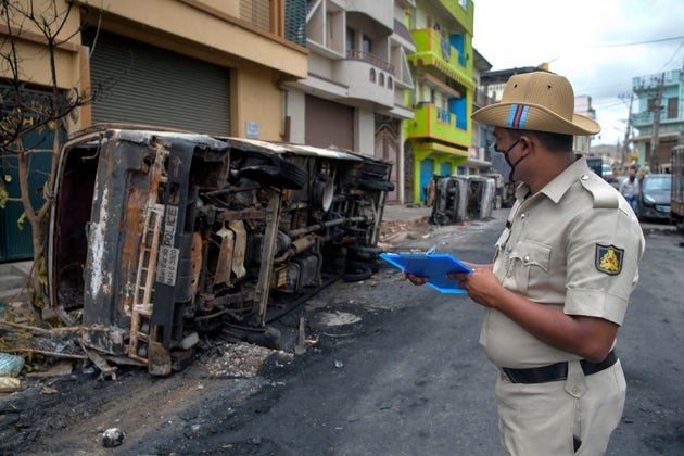 A policeman takes notes next to burnt police vehicles in Bangalore on August 12 after violence broke...