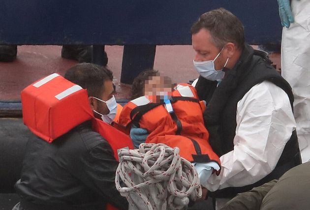 A Border Force officer carries a young child to its father as a group of people thought to be migrants are brought into Dover, Kent, on a Border Force vessel