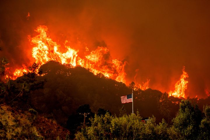 A flag flies as flames from the LNU Lightning Complex fires crest a ridge Tuesday, Aug. 18, 2020, in Napa County, Calif. (AP Photo/Noah Berger)