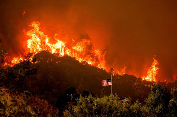 A flag flies as flames from the LNU Lightning Complex fires crest a ridge Tuesday, Aug. 18, 2020, in Napa County, Calif. (AP Photo/Noah Berger)