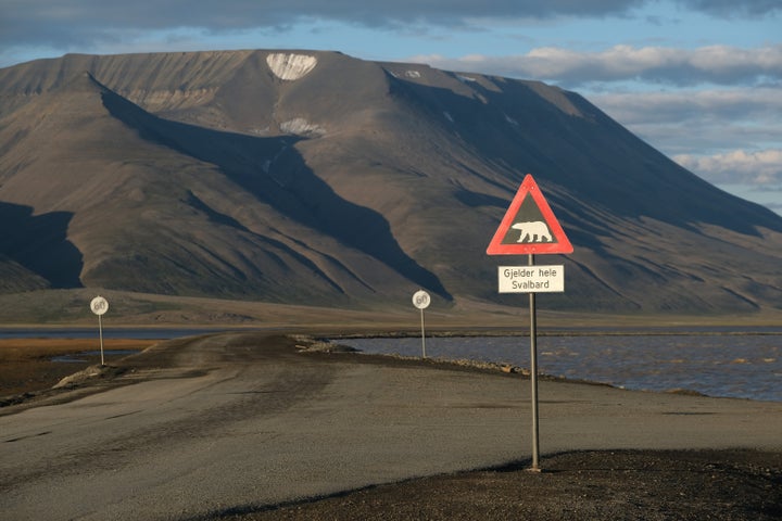 Mountains nearly devoid of snow stand behind a road and a polar bear warning sign during a summer heatwave on Svalbard archipelago on July 29 near Longyearbyen, Norway.