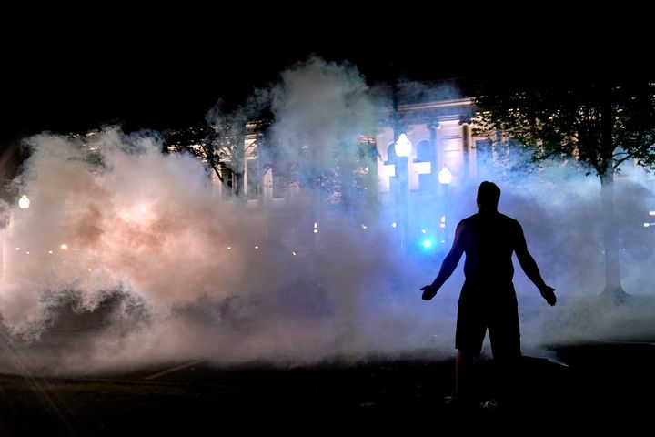 A protester attempts to continue standing through a cloud of tear gas fired by police outside the Kenosha County Courthouse, late Monday.