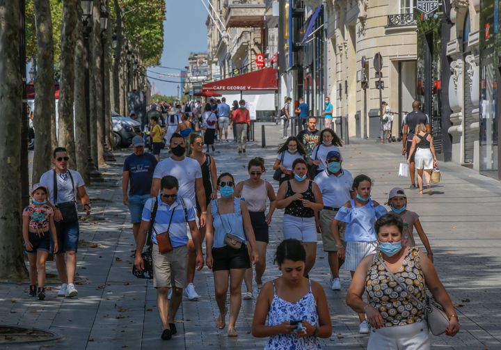 People wearing mask to prevent the spread of COVID-19 stroll along the Champs Elysees avenue in Paris, Sunday, Aug 9, 2020. Paris will make masks mandatory on certain crowded streets and outdoor public areas from Monday following a rise in new COVID-19 cases. (AP Photo/Michel Euler)