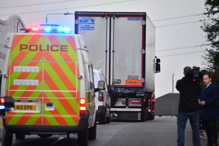 Police officers drive away a lorry, with black plastic visible at the rear, in which 39 dead bodies were discovered.