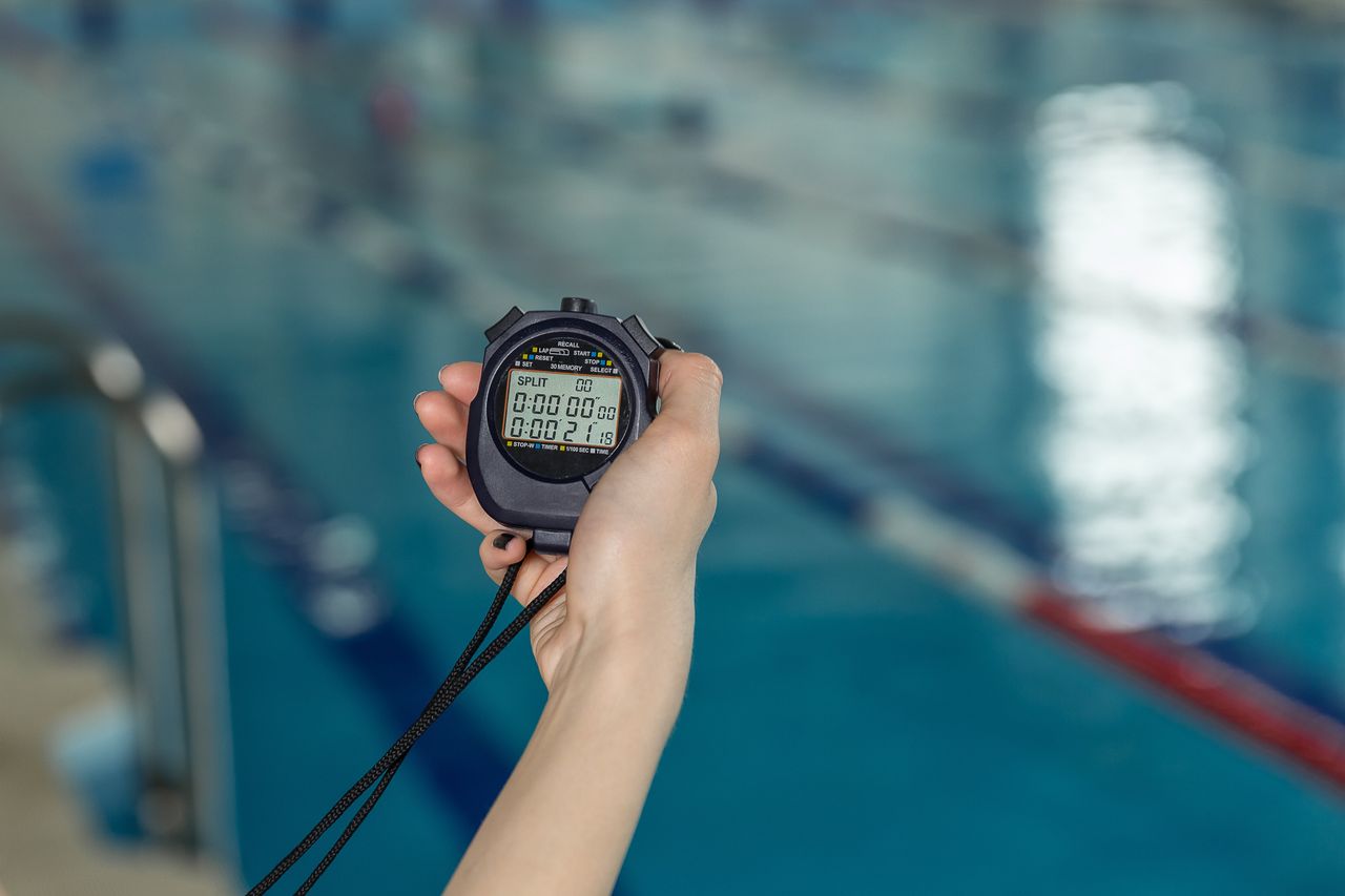 Close-up of coach hand holding stopwatch at poolside.