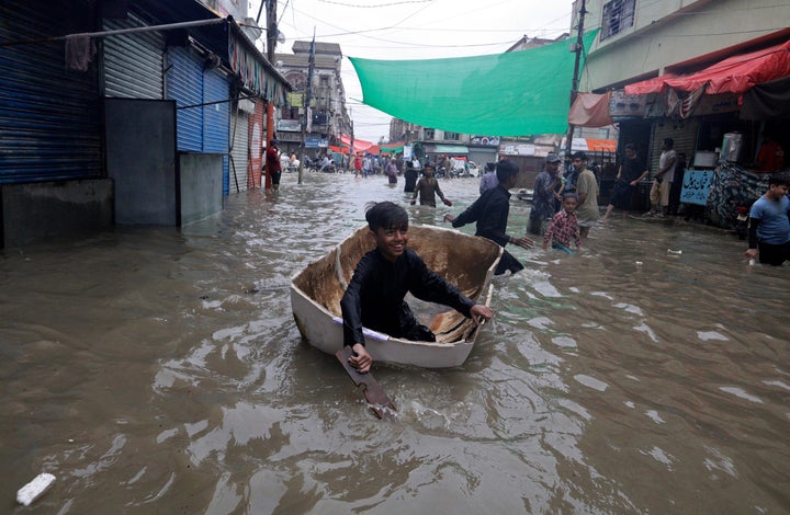 A boy uses half of a fiber tank to navigate a flooded street after heavy monsoon rains, in Karachi, Pakistan, Thursday, Aug.