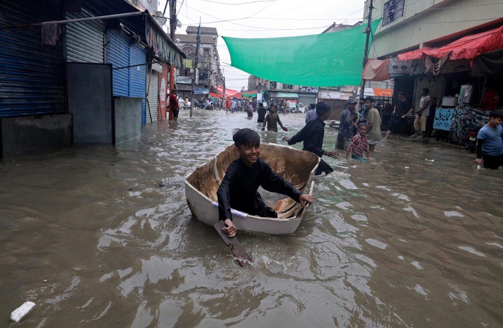 A boy uses half of a fiber tank to navigate a flooded street after heavy monsoon rains, in Karachi, Pakistan, Thursday, Aug. 