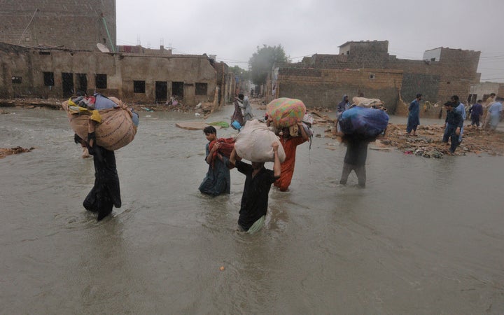 Local residents carry salvaged belongings as they wade through a flooded area during a heavy monsoon rain in Yar Mohammad vil