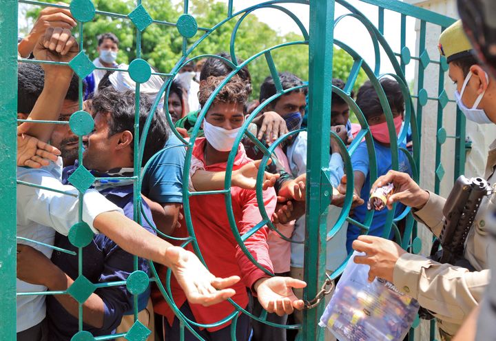 Migrant workers, who were stranded in the central state of Madhya Pradesh due to a lockdown imposed by the government to prevent the spread of coronavirus disease (COVID-19), huddle to receive biscuit packets distributed by police as they wait to leave for their home town, after they arrived in Prayagraj, India, May 1, 2020. REUTERS/Jitendra Prakash