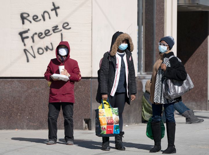 Masked pedestrians wait at a crosswalk in front of graffiti demanding a rent freeze, in Toronto on Thursday, April 2, 2020. 