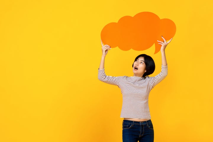 Young Asian woman in casual clothes holding empty speech bubble in colorful yellow studio background