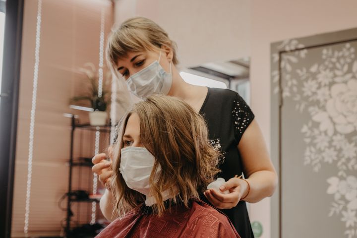 Young woman having her hair cut wearing protective equipment.