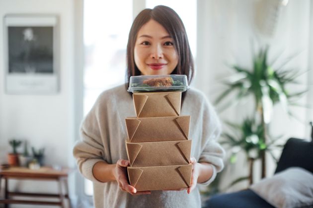 Close up shot of smiling young woman holding a stack of delivery food boxes for sharing.