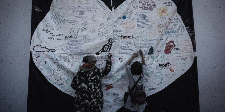 Women write messages on a banner during a memorial service for those who have died from an opioid overdose in Vancouver on Aug. 31, 2017.