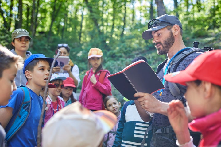 A stock photo of a man reading to kids on a field trip in forest.