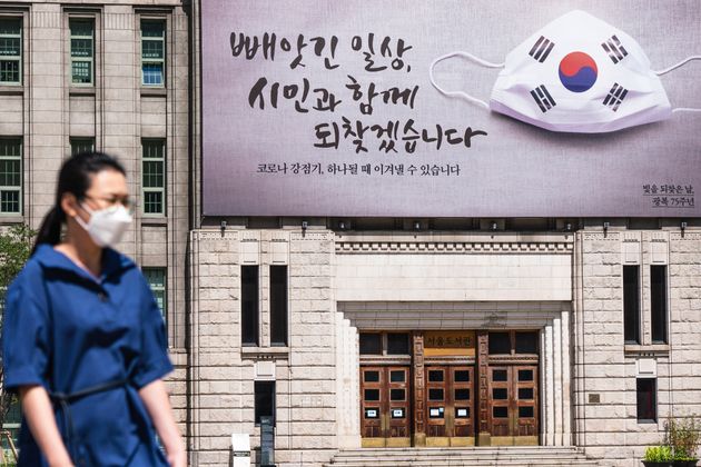 A promotional material recommending the use of a mask posted on the outer wall of Seoul City Hall.  Year 2020