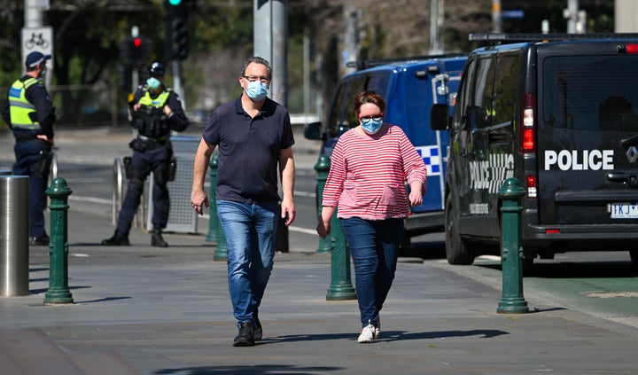 A couple takes a walk as police look on in Melbourne on September 6, 2020 as the state announced an extension to its strict lockdown law while it battles fresh outbreaks of the COVID-19 coronavirus.