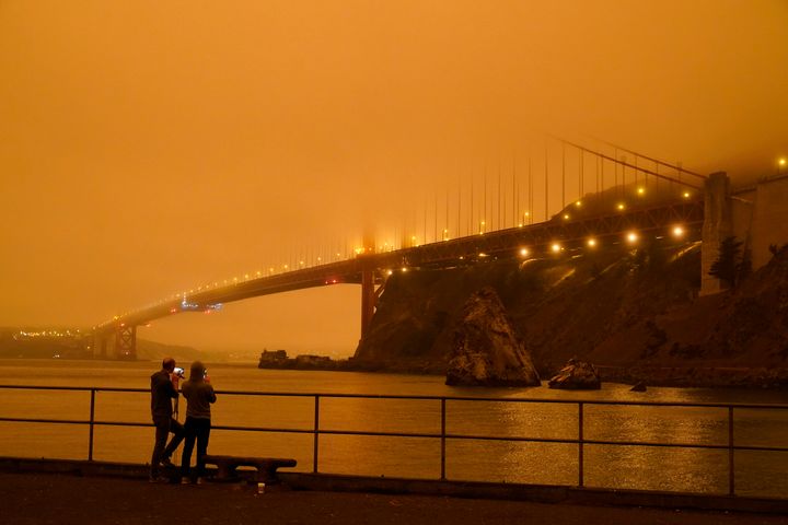 Patrick Kenefick, left, and Dana Williams, record the darkened Golden Gate Bridge covered with smoke from wildfires.