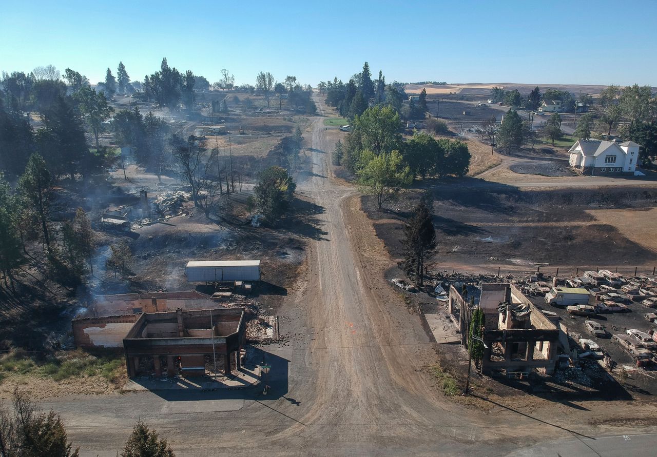 In downtown Malden, Washington, the former post office at lower left and another historic building at lower right still smolder Tuesday, a day after a fast-moving wildfire swept through the tiny town west of Rosalia.