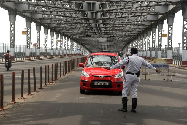 A Kolkata police personnel stops a car on Howrah Bridge amid a weekly complete lockdown imposed by the...