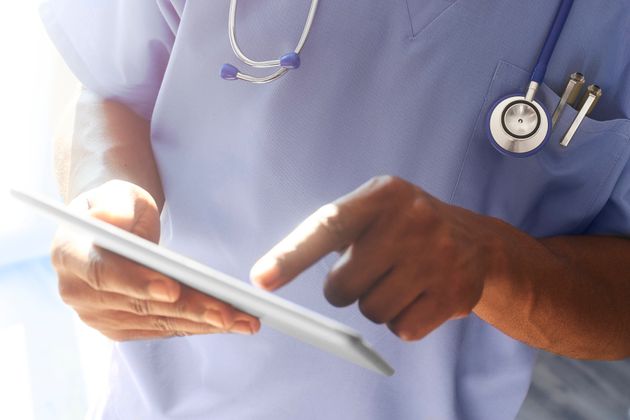 Doctor or surgeon stood in hospital ward using digital tablet