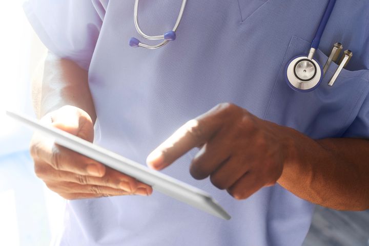 Doctor or surgeon stood in hospital ward using digital tablet