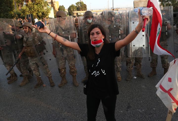 An anti-government protester tries to calm down other protesters, as she stands in front of Lebanese soldiers who bloc a road that links to the presidential palace, during a protest against the Lebanese President Michel Aoun, in Baabda east of Beirut, Lebanon, Saturday, Sept. 12, 2020. (AP Photo/Bilal Hussein)