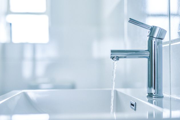 Photo of an open tap with running water in a bathroom in