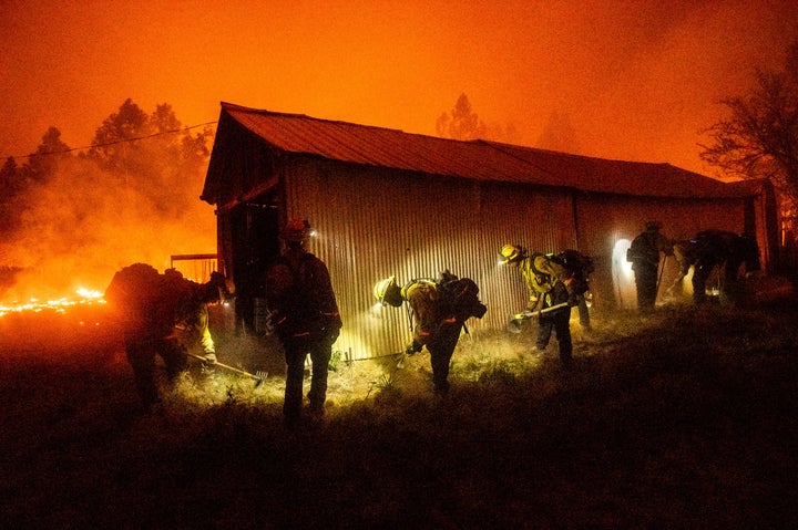 A hand crew clears vegetation from around a barn as the Bear Fire burns through the Berry Creek area of Butte County, Calif.,