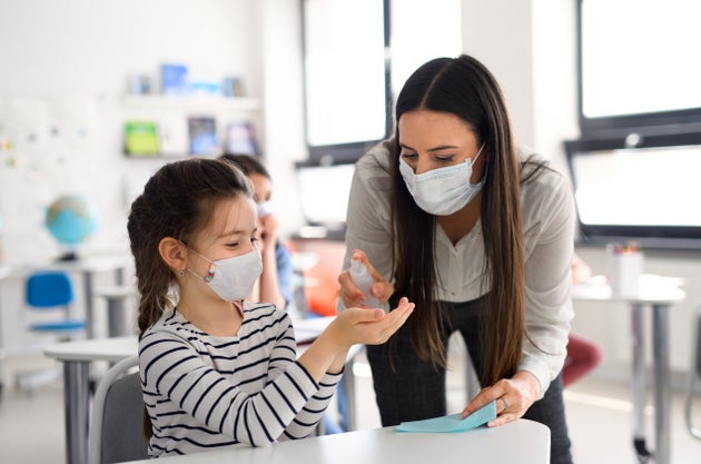 Teacher and children with face mask back at school after lockdown, disinfecting hands.