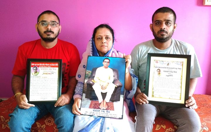 Anindita Mitra, 61, flanked by her sons Satyajit Mitra, right and Abhijit Mitra, pose with portraits of her husband late Narayan Mitra, at her house in Silchar, India, Sunday, Sept. 13, 2020. Narayan Mitra, wasn't listed among those killed by the coronavirus that authorities put out daily because the test results confirming COVID-19 arrived after his death.