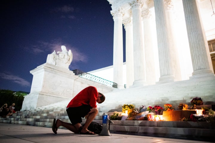 A man kneels outside the Supreme Court before tributes to the Justice Ruth Bader Ginsburg following her death on Friday.