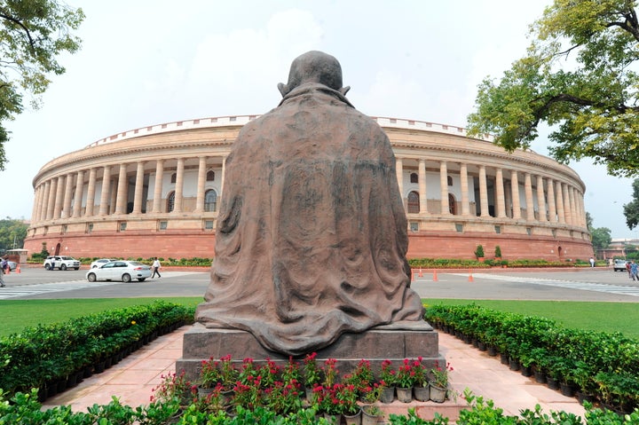 A Mahatma Gandhi statue overlooks the Parliament building as law makers arrive in New Delhi, Sept.14, 2020. 