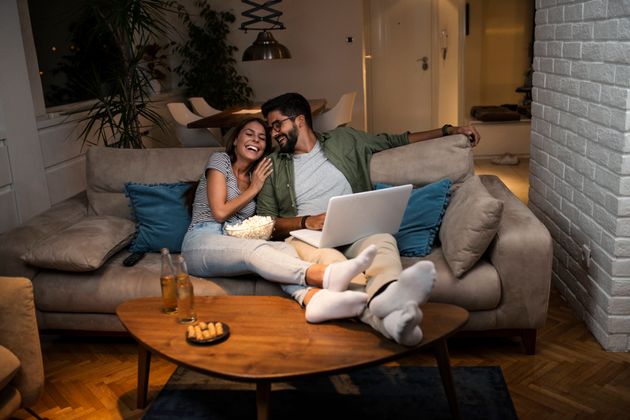 The couple is lying on the sofa and watching the YouTube on the laptop.