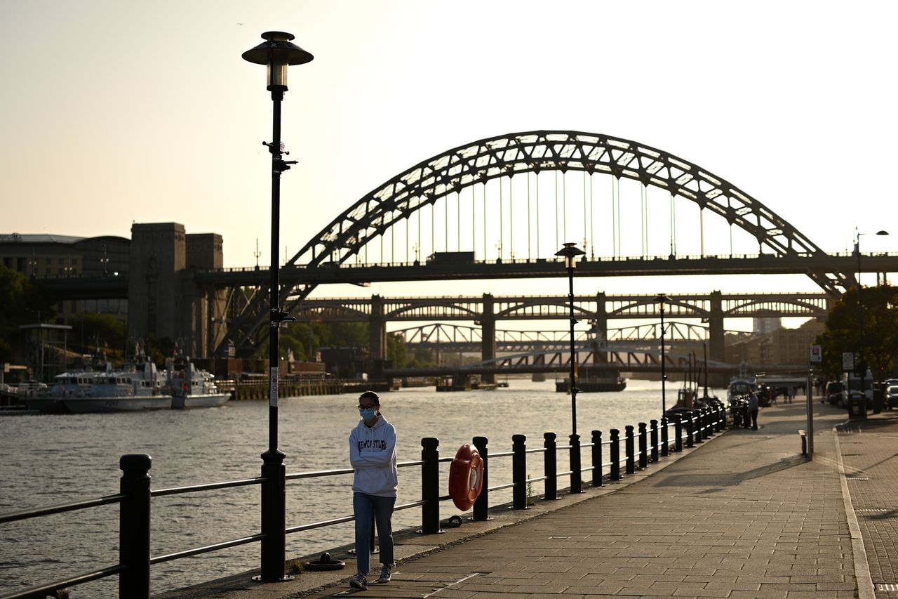 A woman wearing a protective face mask walks along the quayside, on the banks of the River Tyne, backdropped by the Tyne Bridge in Newcastle. 