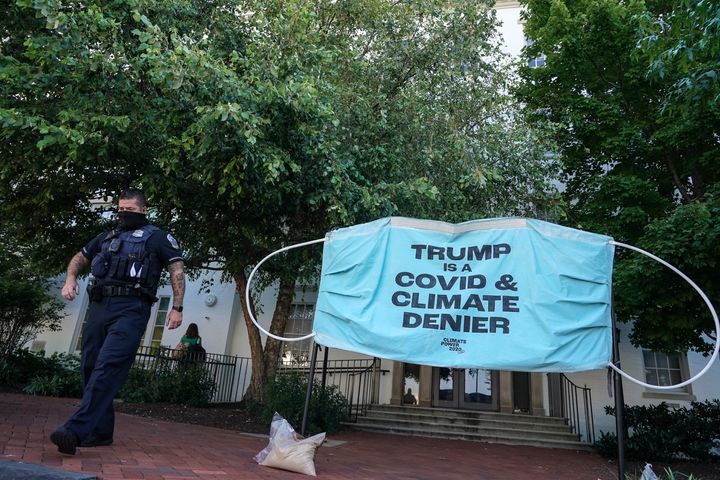 A police officer walks past a protest banner berating President Donald Trump as denying the science behind the COVID-19 pandemic and climate change set up in front of the Republican National Convention headquarters on Aug. 24 in Washington. No signs have surfaced that Trump has changed his tune.