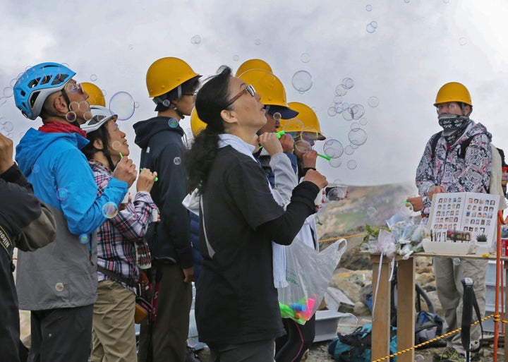 御嶽山の剣ケ峰で、献花台を囲みシャボン玉を飛ばす遺族＝2018年9月26日