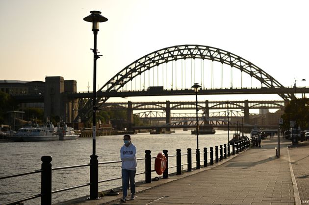 A woman wearing a protective face mask walks along the quayside, on the banks of the River Tyne, backdropped by the Tyne Bridge in Newcastle, north-east England