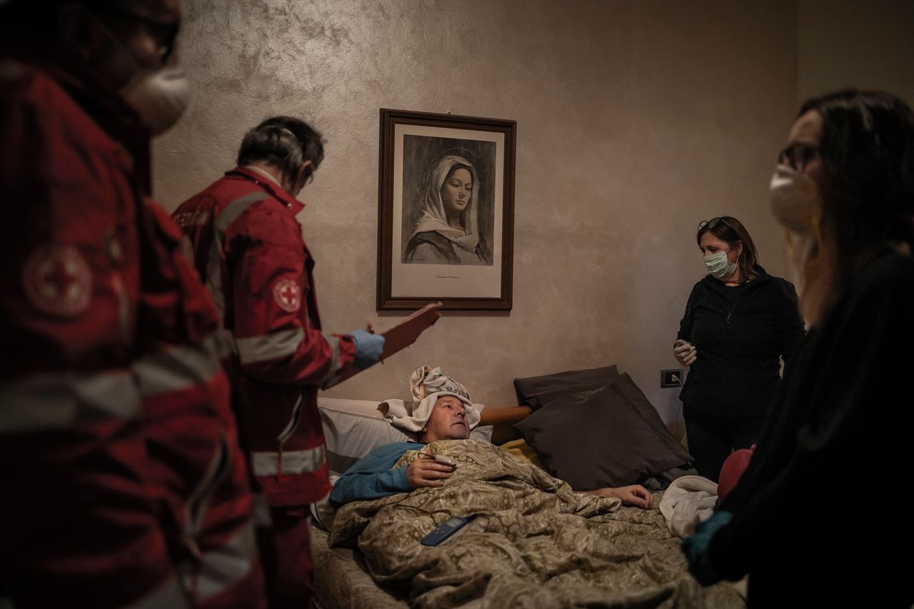 Ο Κλαούντιο Τραβέλι (61), ασθενής με Covid-19, αναπαύεται στο κρεβάτι του μετά από την εξέταση από τους εθελοντές του Διεθνούς Ερυθρού Σταυρού, 15 Μαρτίου 2020, στο Κάτω Τσενάτε στο Μπέργκαμο της Ιταλίας. Μετά την εξέτασή του ο Travelli αποφασίζει να παραμείνει σπίτι. Την επόμενη μέρα η οικογένειά του αποφασίζει να καλέσει ασθενοφόρο επειδή η κατάστασή του χειροτερεύει. Ο Claudio εισήχθη στο νοσοκομείο και παρέμεινε στην ΜΕΘ και ΜΑΦ για τρεις εβδομάδες και πήρε εξιτήριο στις 3 Απριλίου.
